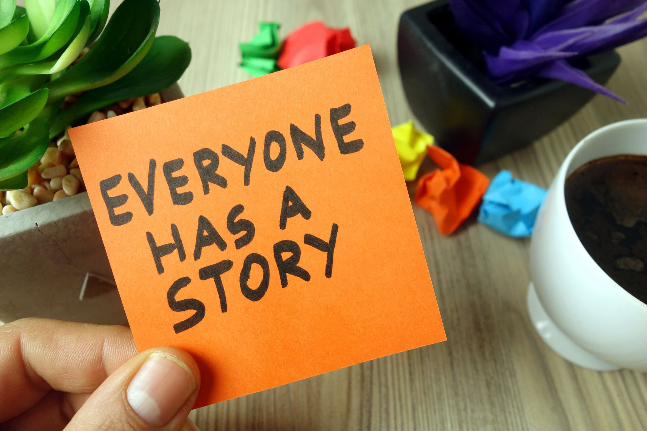 A person is holding an orange post it note, saying, 'everyone has a story'.