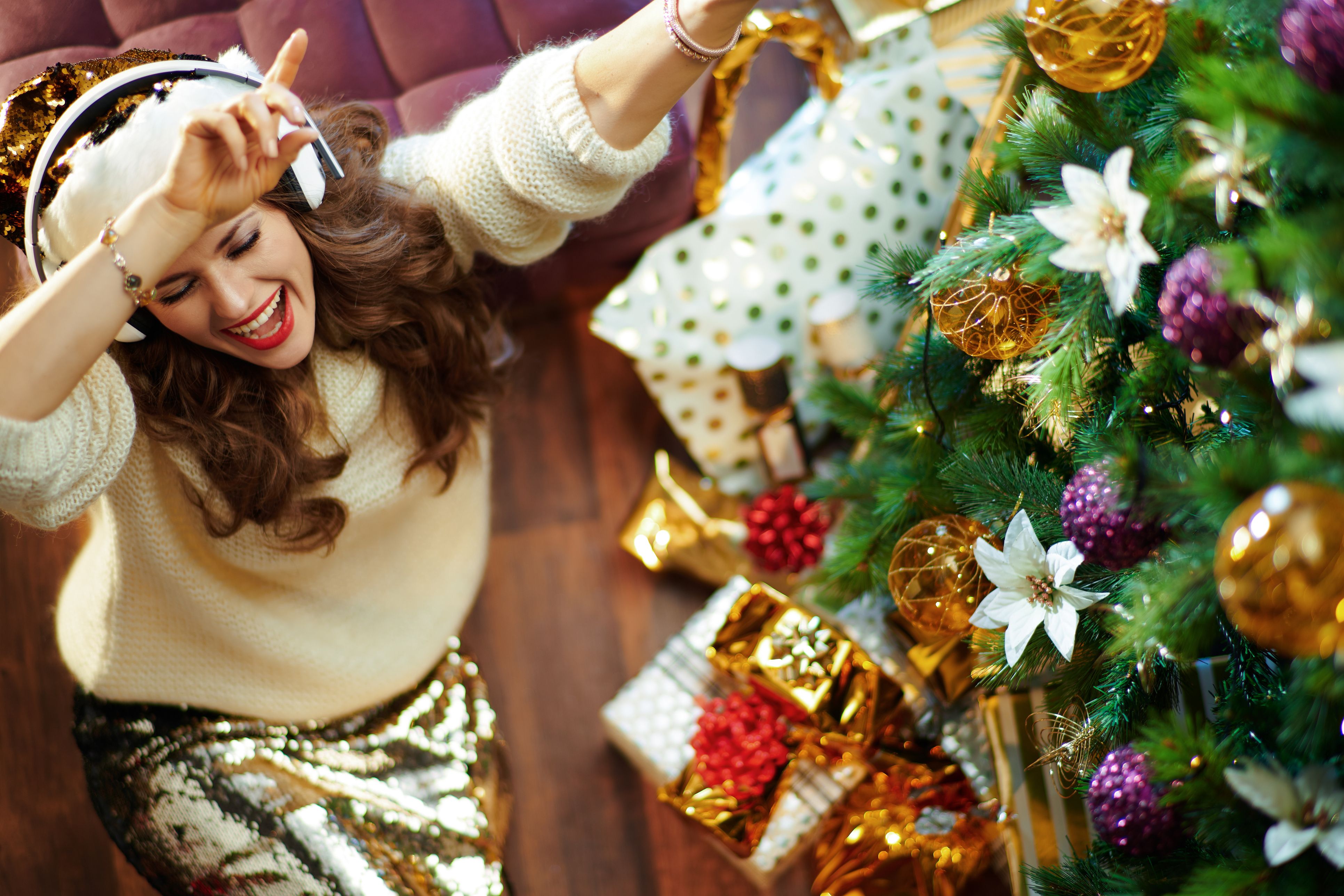A female sat next to a Christmas tree listening to music through headphones.